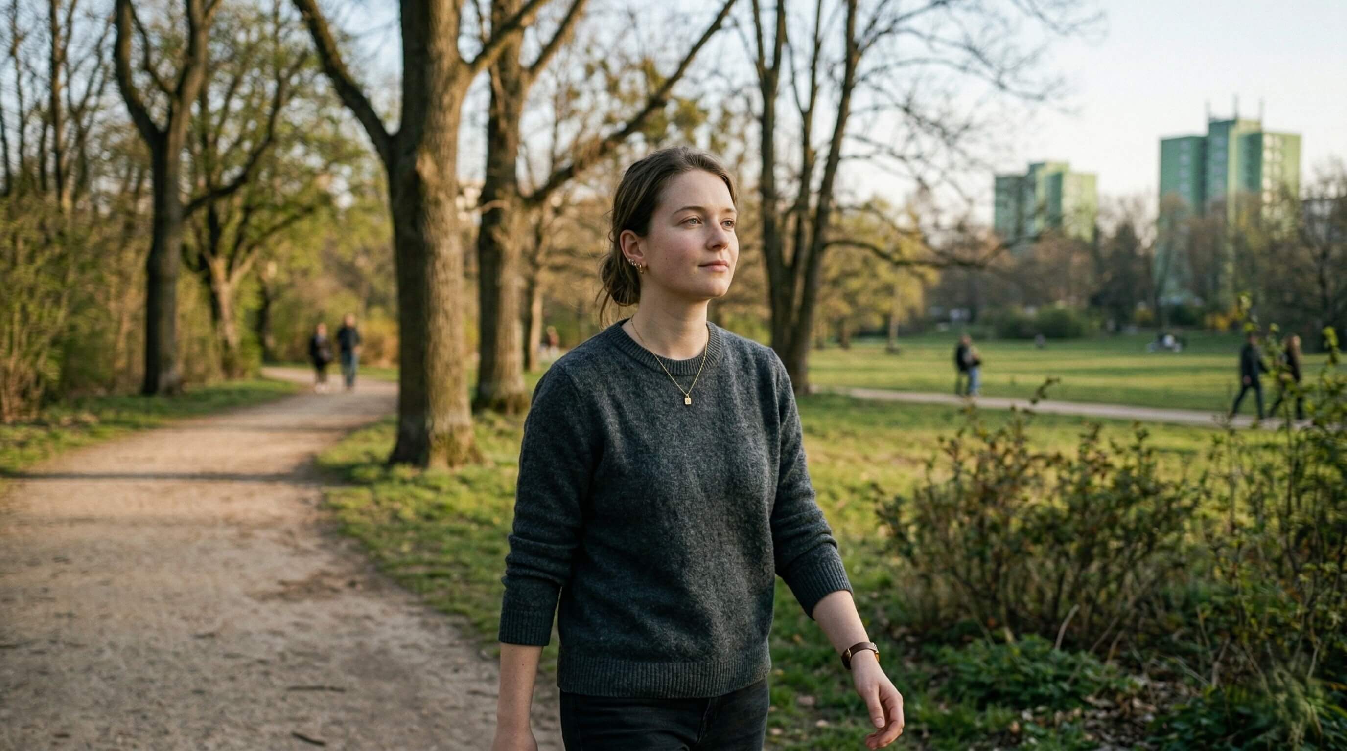 Woman walking in an urban park with a calm expression and steady posture, conveying a sense of direction and inner stability.